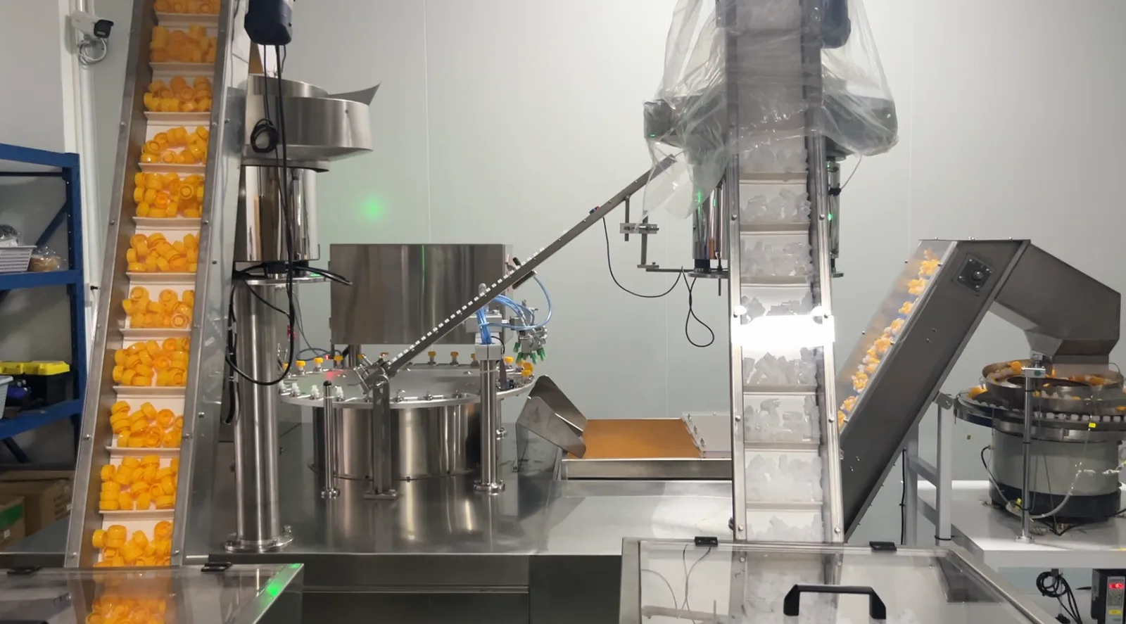 Orange plastic caps climbing two inclined conveyors toward a rotary feed table at a closure moulding plant