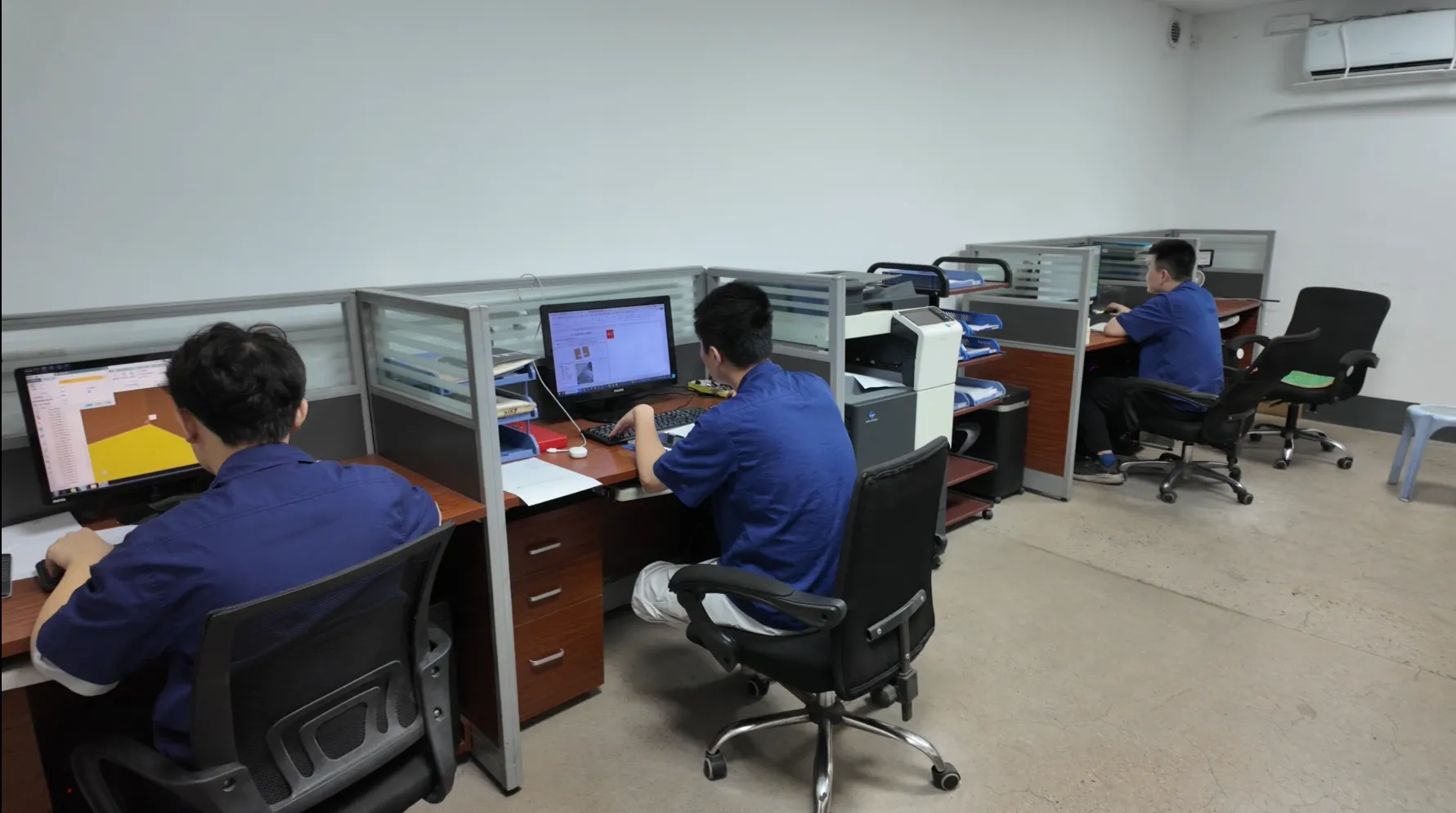 Engineers at design-office workstations, one reviewing a CAD drawing of a molded part on screen
