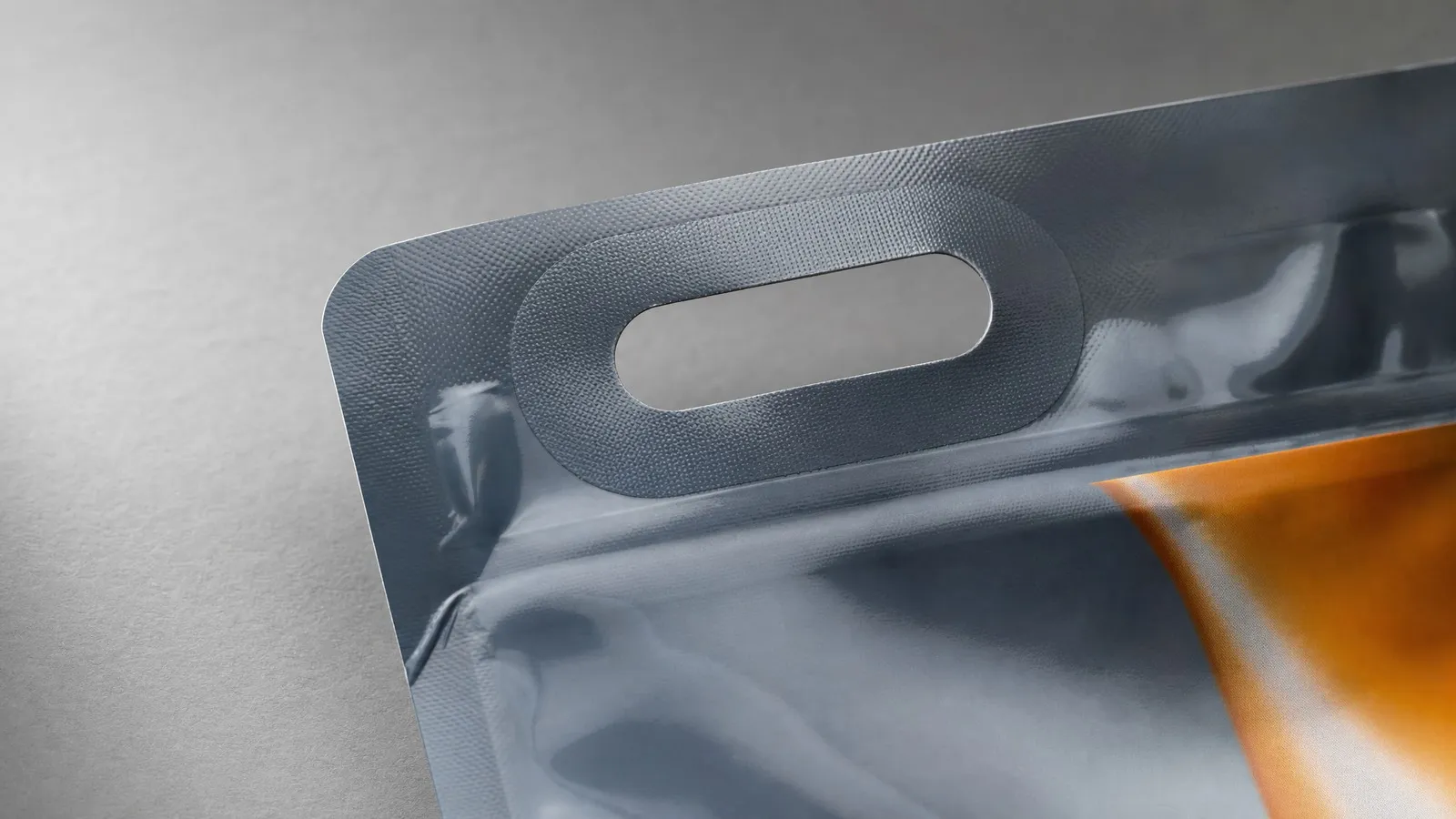A close-up of an oval aperture die-cut through laminated pouch film, with a thicker reinforcement patch welded around the opening