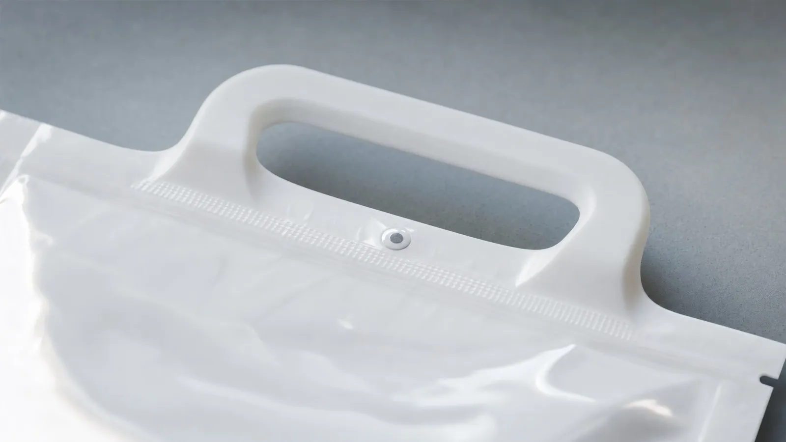 A white injection-molded pouch handle attached to stand-up pouch film, with the weld band along its base and a rivet through the film