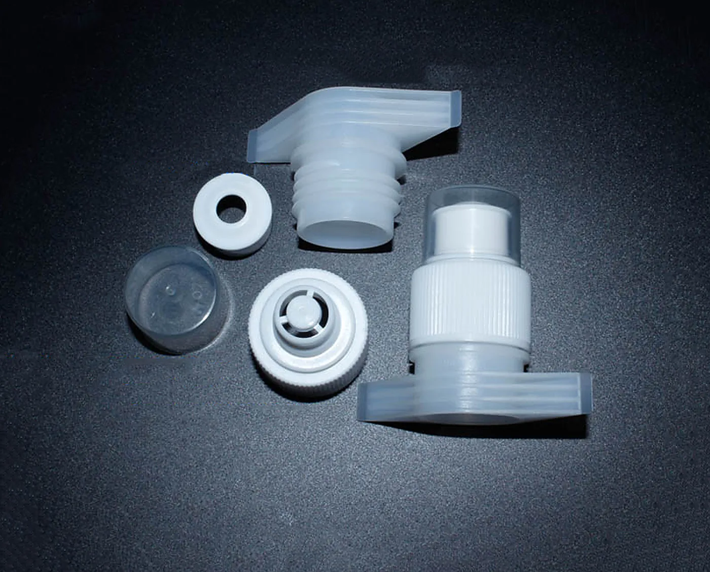 The push-pull cap assembly separated into stem, body, seal and dust cap on a dark surface