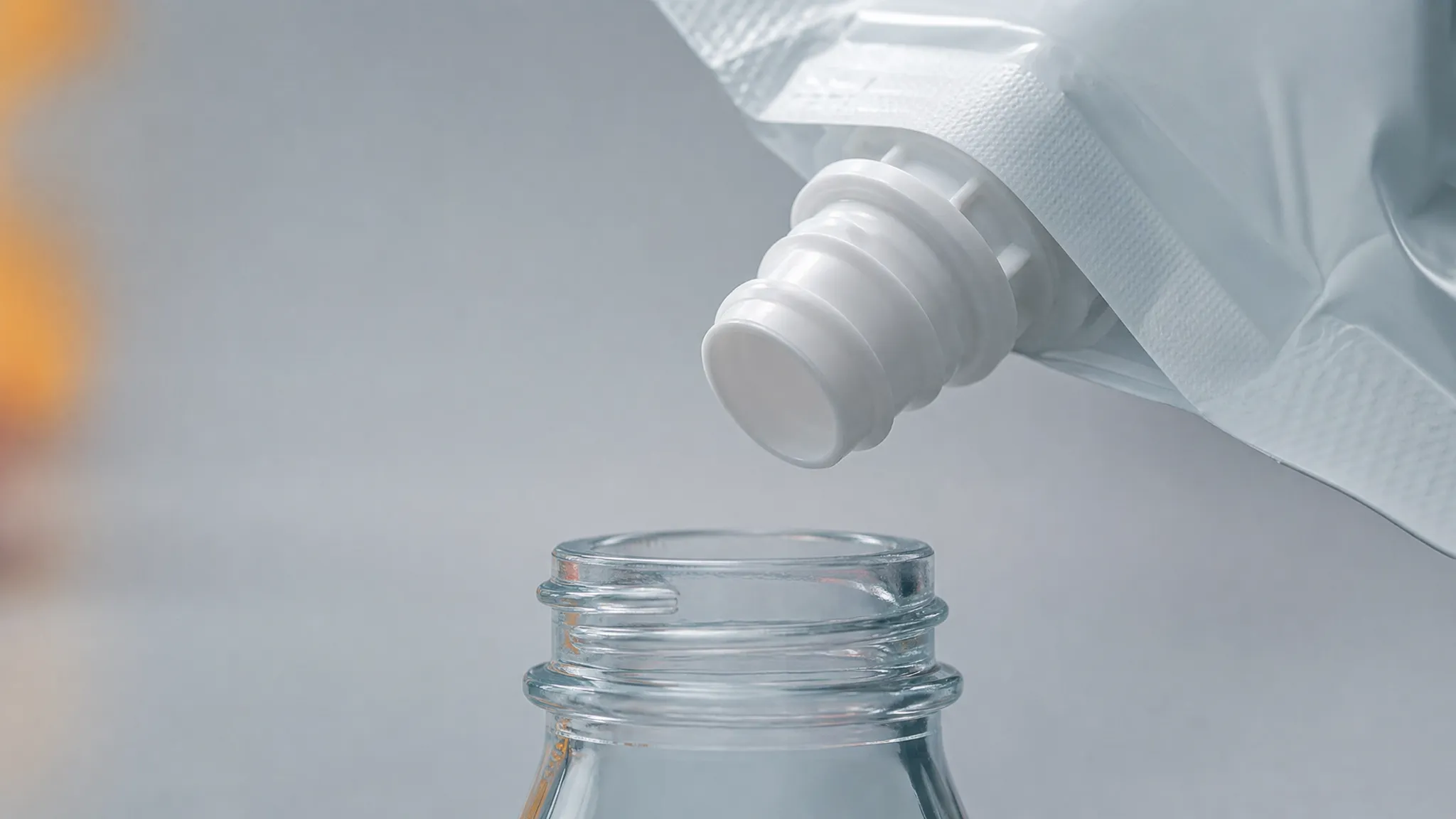 A close-up of a pouch spout outlet held just above a bottle opening, with a visible gap between the two parts